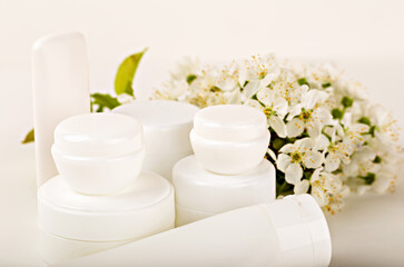 Various white skincare containers placed in front of delicate white flowers, representing purity and cleanliness. Ideal for beauty, skincare and wellness promotions