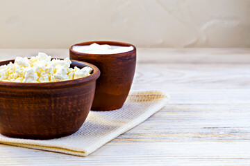 Close up of cottage cheese and sour cream served in rustic clay bowls on light wooden table. Perfect for illustrating traditional dairy products and healthy eating