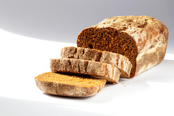 Loaf of dark freshly baked bread with slices on a white background in the sunlight