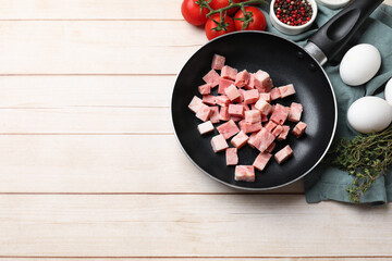 Pieces of fresh bacon in frying pan and products on light wooden table, flat lay. Space for text