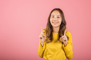 Asian happy portrait beautiful young woman standing makes gesture two fingers point upwards above presenting product something, studio shot isolated on pink background with copy space, point up