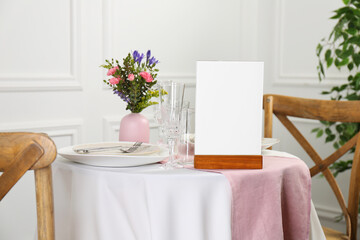 Menu holder, clean dishware and vase with beautiful flowers on white table in restaurant