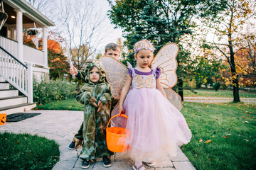 Kids in fairy and dinosaur costumes trick-or-treat outside