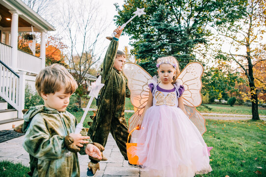 Three children in fairy and dinosaur costumes playing outside