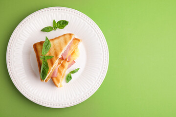 Pieces of toasted bread with melted cheese, ham and basil on green background, top view. Space for text