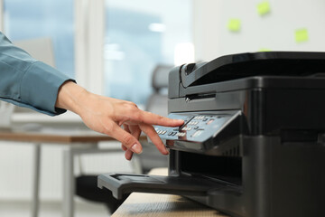 Woman using modern printer at workplace indoors, closeup