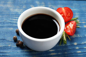 Balsamic vinegar, tomatoes, peppercorns and rosemary on blue wooden table, closeup