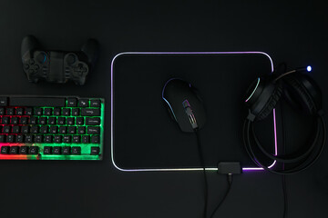 Computer mouse, headset, RGB keyboard and game controller on black background, flat lay