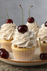 Delicious cupcakes with cream and cherries on wooden table, closeup