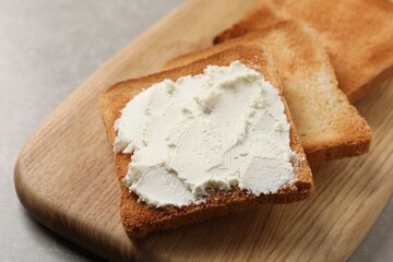 Delicious toasted bread slices with cream cheese on grey table, closeup