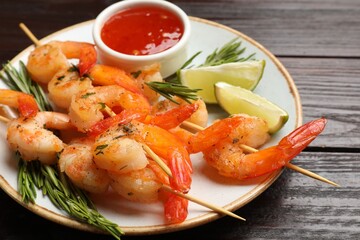Delicious grilled shrimp skewers served with sauce and lime on wooden table, closeup