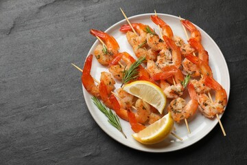 Skewers with delicious grilled shrimps served on black table, top view. Space for text