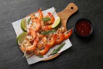 Delicious grilled shrimp skewers served with sauce and lime on black table, top view