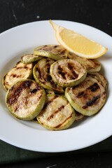 Tasty grilled zucchini slices with lemon on black table