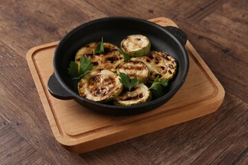 Tasty grilled zucchini slices with parsley in dish on wooden table