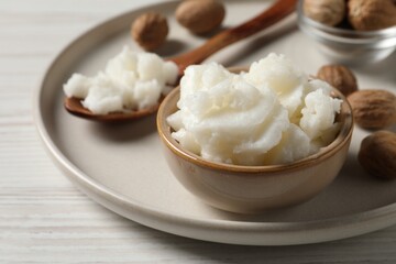 Shea butter in bowl and nuts on white wooden table, closeup