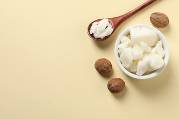 Shea butter in bowl, spoon and nuts on beige background, flat lay. Space for text