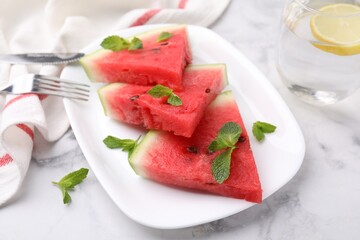 Fresh watermelon slices with mint leaves and glass of water on white marble table, closeup