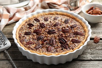 Delicious pecan pie in baking dish and cake server on wooden table, closeup