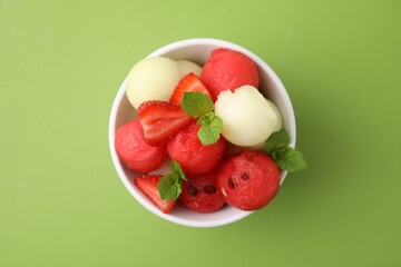 Tasty watermelon and melon balls with strawberries in bowl on green table, top view