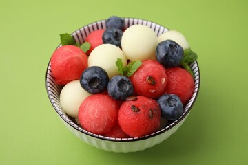 Tasty watermelon and melon balls with blueberries in bowl on green table, closeup