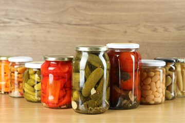 Different pickled products in jars on wooden table