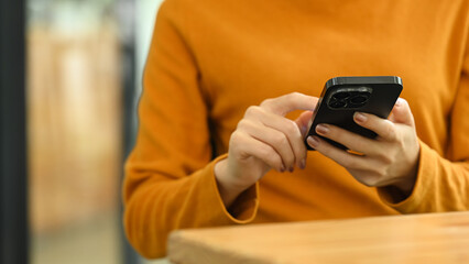 Young woman in yellow sweater hands texting on a smartphone. Technology and communication concept