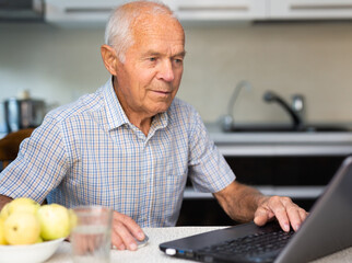 Elderly man carefully examines the possibilities of buying cryptocurrency over Internet using laptop