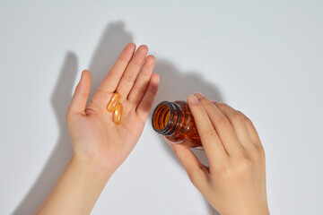 A person holding a brown jar of vitamins in one hand and pouring yellow capsules onto another, over white background. Top view photo, empty space for adding text SUPPLEMENT CONCEPT
