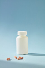 Simple and elegant layout with pharmaceutical concept, a white bottle without label isolated on blue background, in front of it is a few capsules scattered. Front view, copy space
