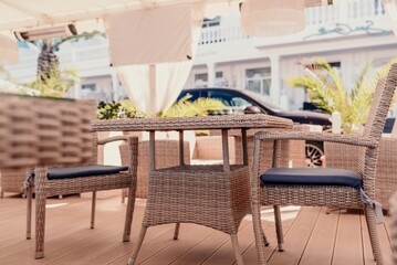 Wicker furniture tables in the open air are waiting for visitors. The interior of the restaurant in the open air. Empty tables of street cafe.