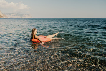 A woman is floating on a red inflatable raft in the ocean