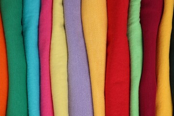 Stack of clean colorful t-shirts as background, closeup