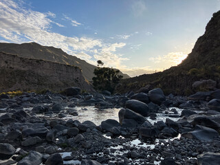 Majestic gray rocky landscape with a serene river winding through. A vibrant sunset casts a warm glow, highlighting the rugged terrain. Perfect for nature, travel, and adventure themes. Stunning.