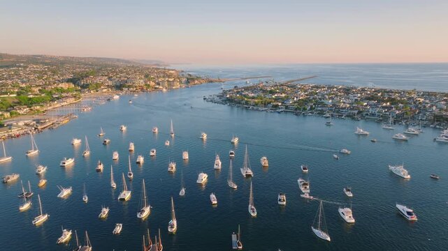 Newport Beach, California offers a stunning aerial view with a bustling harbor, boats, coastline, and a clear sunset sky, combining coastal leisure and urban living in picturesque scenery