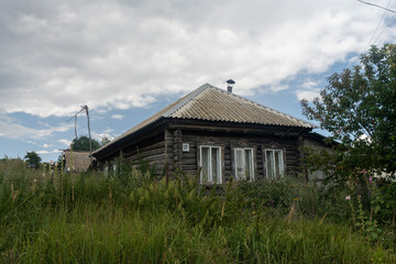 Wooden house in a Russian village with green grass and flowers against a blue sky with white clouds