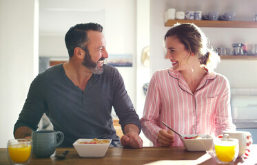 Happy couple, laughing or eating breakfast with cereal, diet or juice in morning meal in home kitchen. People, trust or snack in bowl for bonding, funny joke and food in healthy marriage together