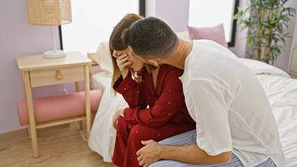A man consoles a distressed woman, both seated on a bed in a well-lit bedroom, evoking emotions of...