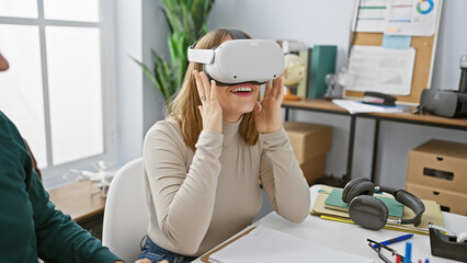 A woman experiencing virtual reality with a headset in a modern office beside a male colleague.