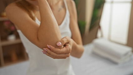 A woman with manicured hands touches her elbow in a serene spa room, capturing a moment of wellness and relaxation indoors.