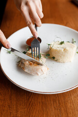 sweet girl is eating а delicious dish with juicy chicken, fragrant herbs, and tomato sauce on a beautiful white plate in a cozy nice restaurant