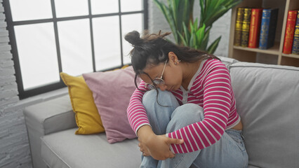 Hispanic woman contemplating indoors on a couch, evoking a serene, introspective mood within a cozy...