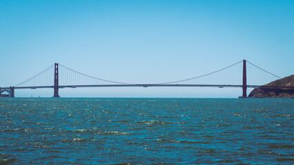 Fototapeta premium the Golden Gate Bridge spanning across the water on a clear, sunny day. The bridge’s iconic red towers and suspension cables are visible, with the blue sky and ocean in the background.