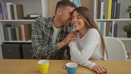 A loving man kissing a smiling woman's cheek in a cozy living room with colorful mugs on the table.