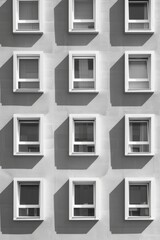 A minimalist photograph featuring a repeating sequence of industrial windows on a modern building, creating a rhythmic pattern that emphasizes both unity and variation. The image explores the balance 