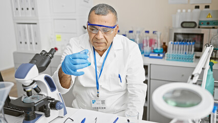 Hispanic man in lab coat examines specimen in a laboratory setting.
