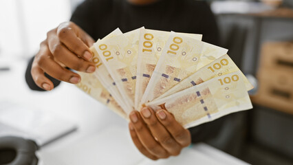 African american woman holding danish currency in an office setting, representing financial...