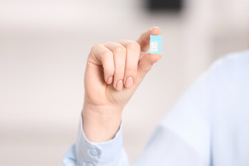 Woman holding modern SIM card indoors, closeup