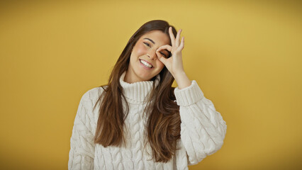 A joyful young woman makes an okay gesture with her hand against a vibrant yellow background.