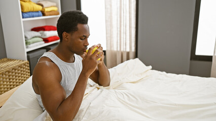A young adult black man drinking coffee in a cozy, well-lit bedroom interior, exhibiting a relaxed...
